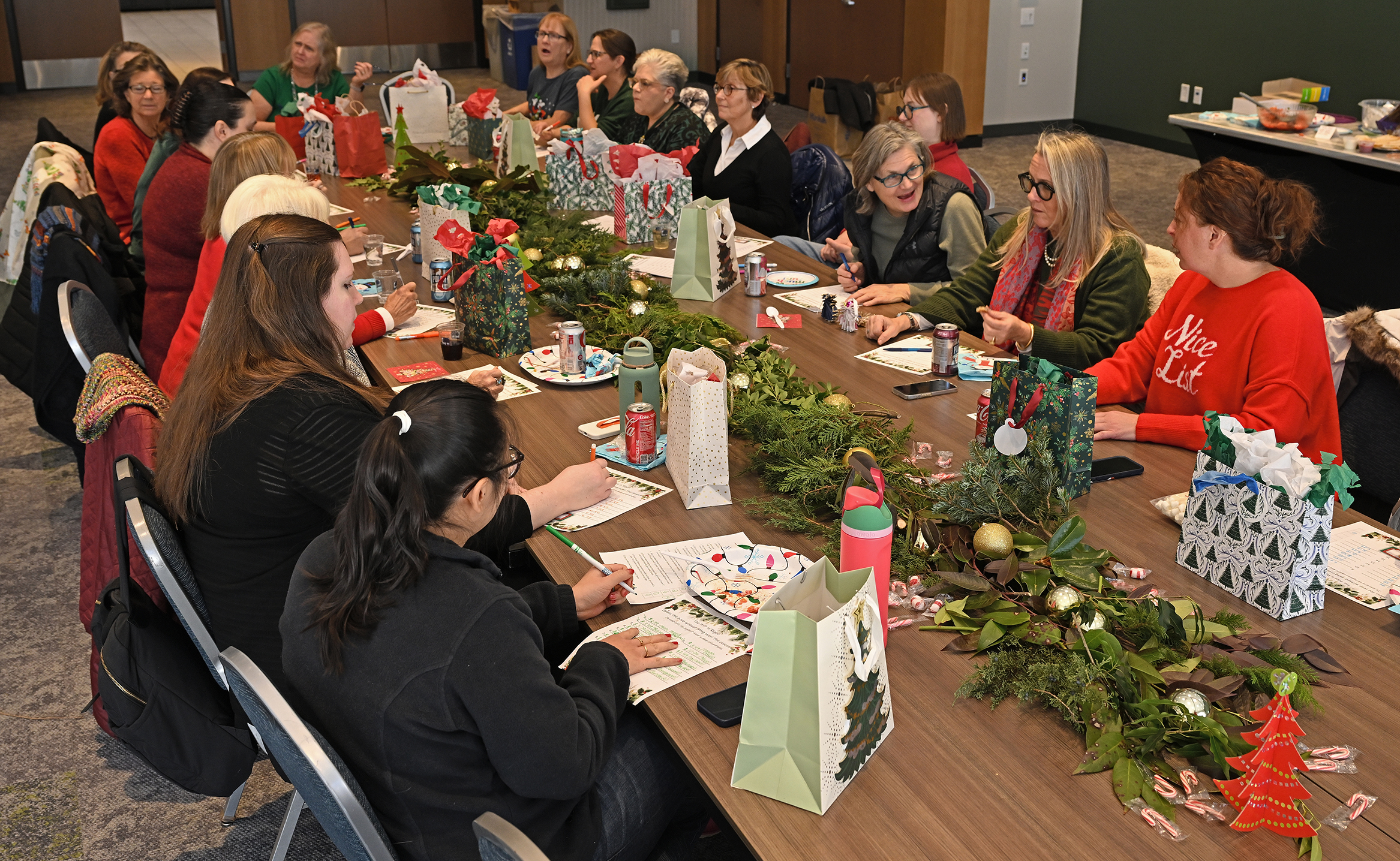 A group of college staff in dressed in Christmas holiday garb gather around a table for a luncheon.