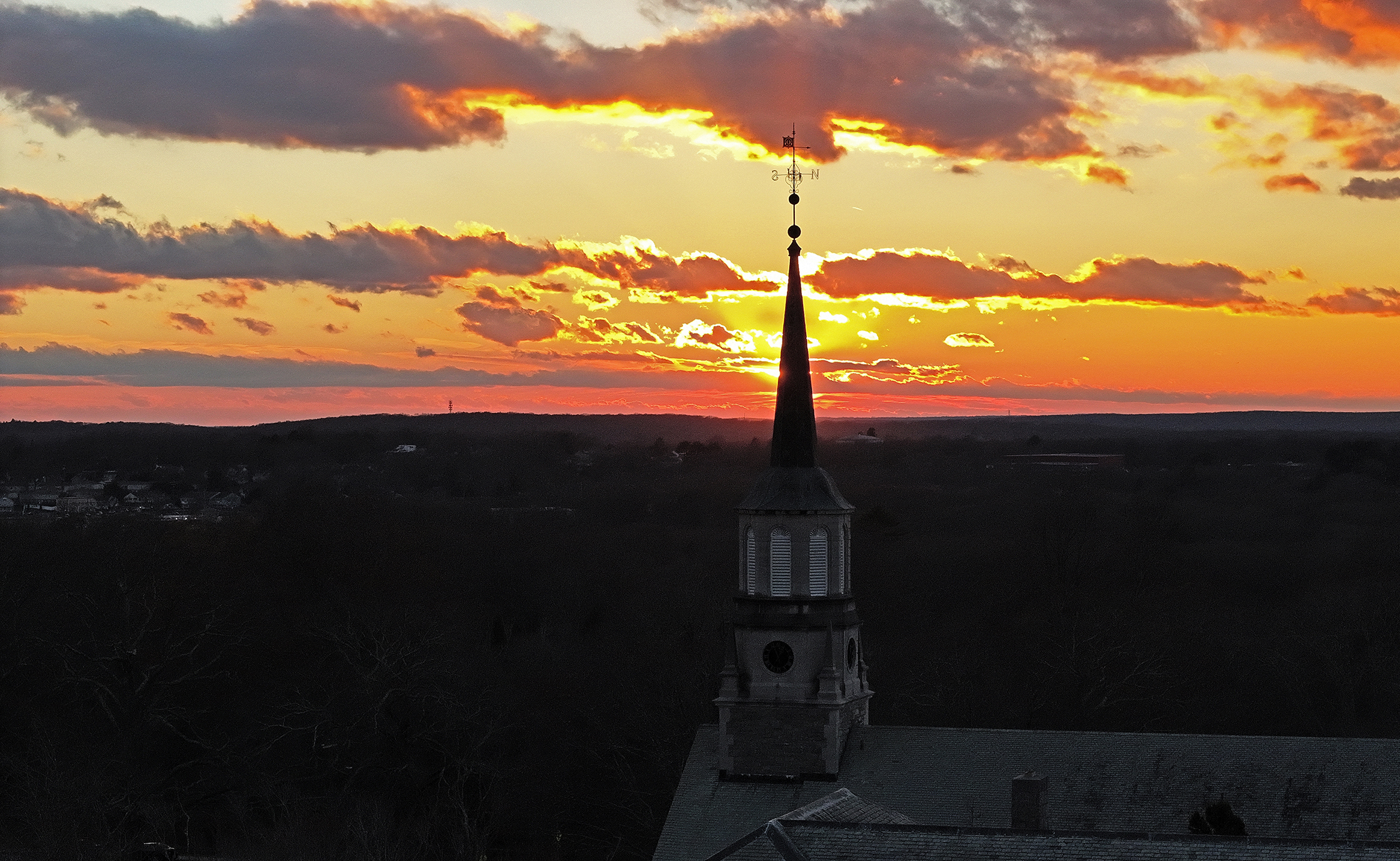 A college chapel steeple stands in silhouette with a red, orange, and yellow sunset sky.