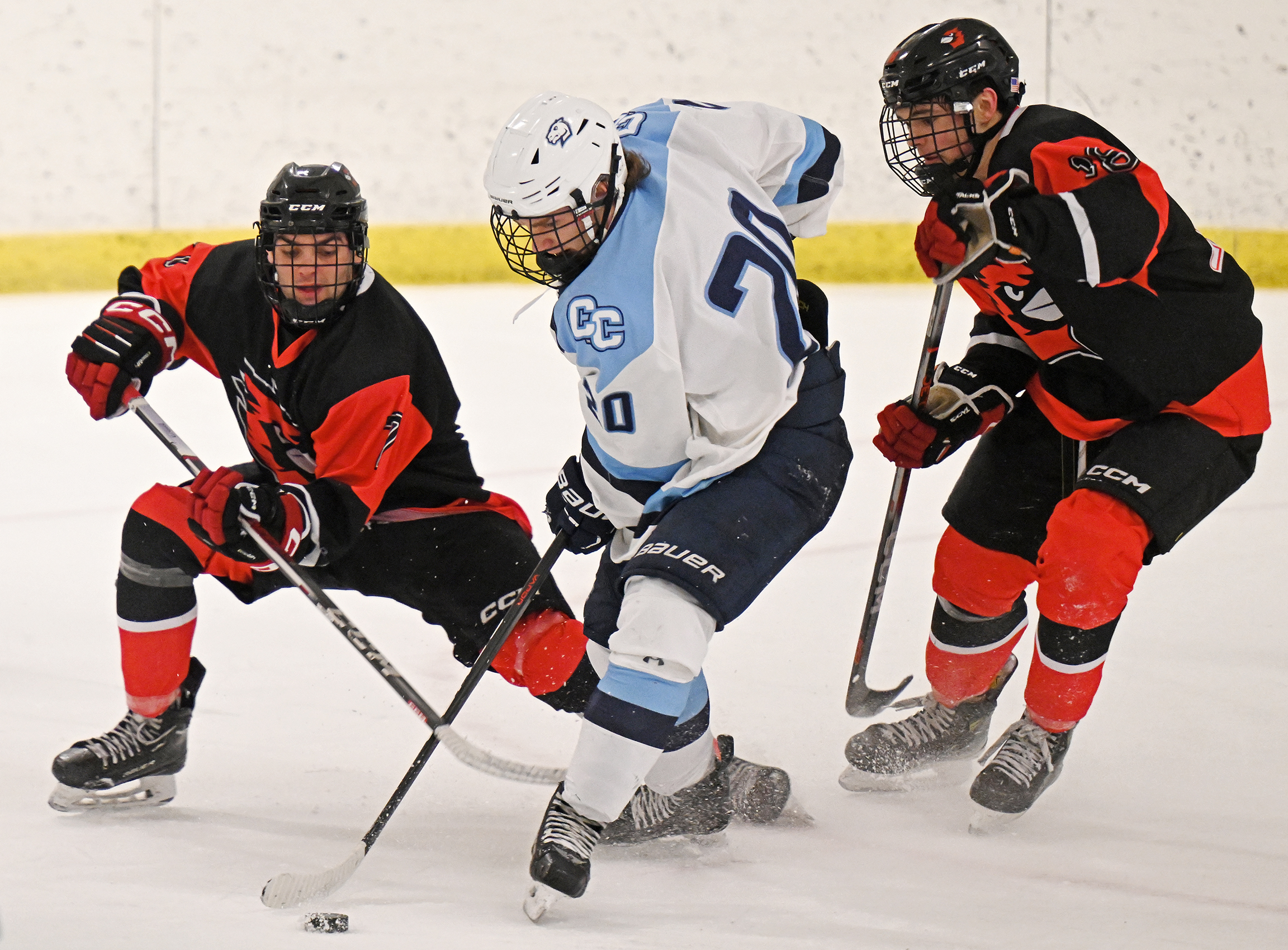 A hockey player in blue and white battles for possession of the puck between two defenders wearing orange and black.