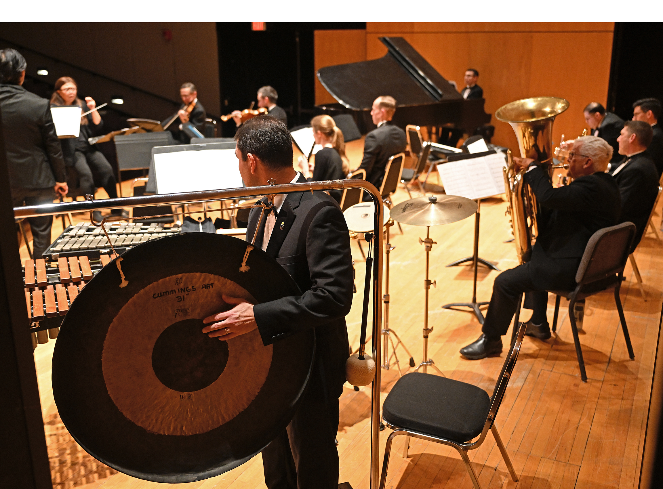 A chamber orchestra percussionist plays the gong as seen from backstage during a performance.