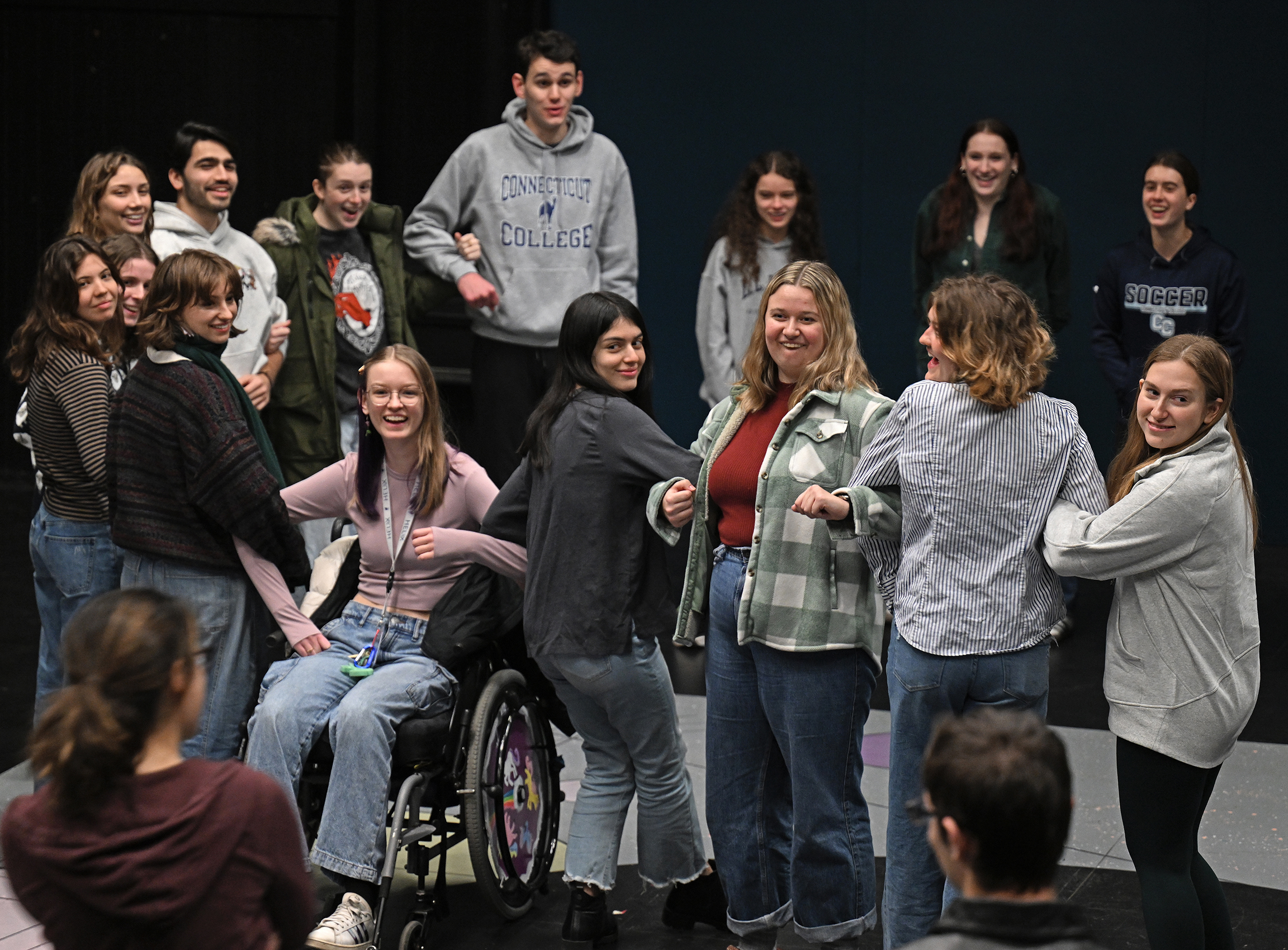 Actors link arms as they gather on stage for a team-building activity in a black box theater.