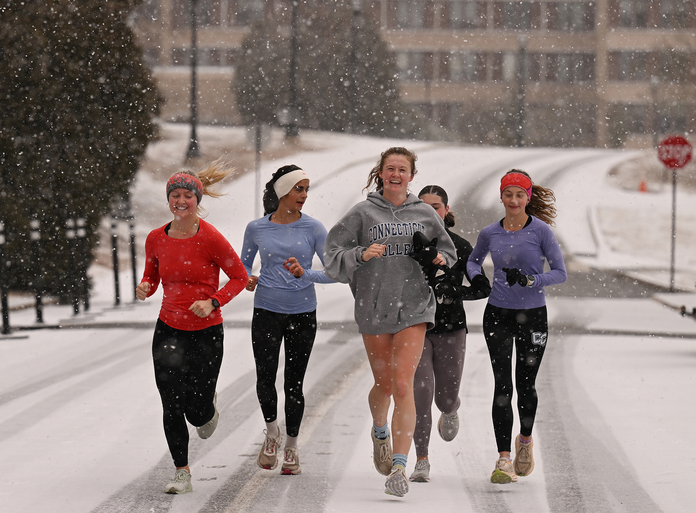 A group of female students run down a snow-covered road as snow continues to fall.