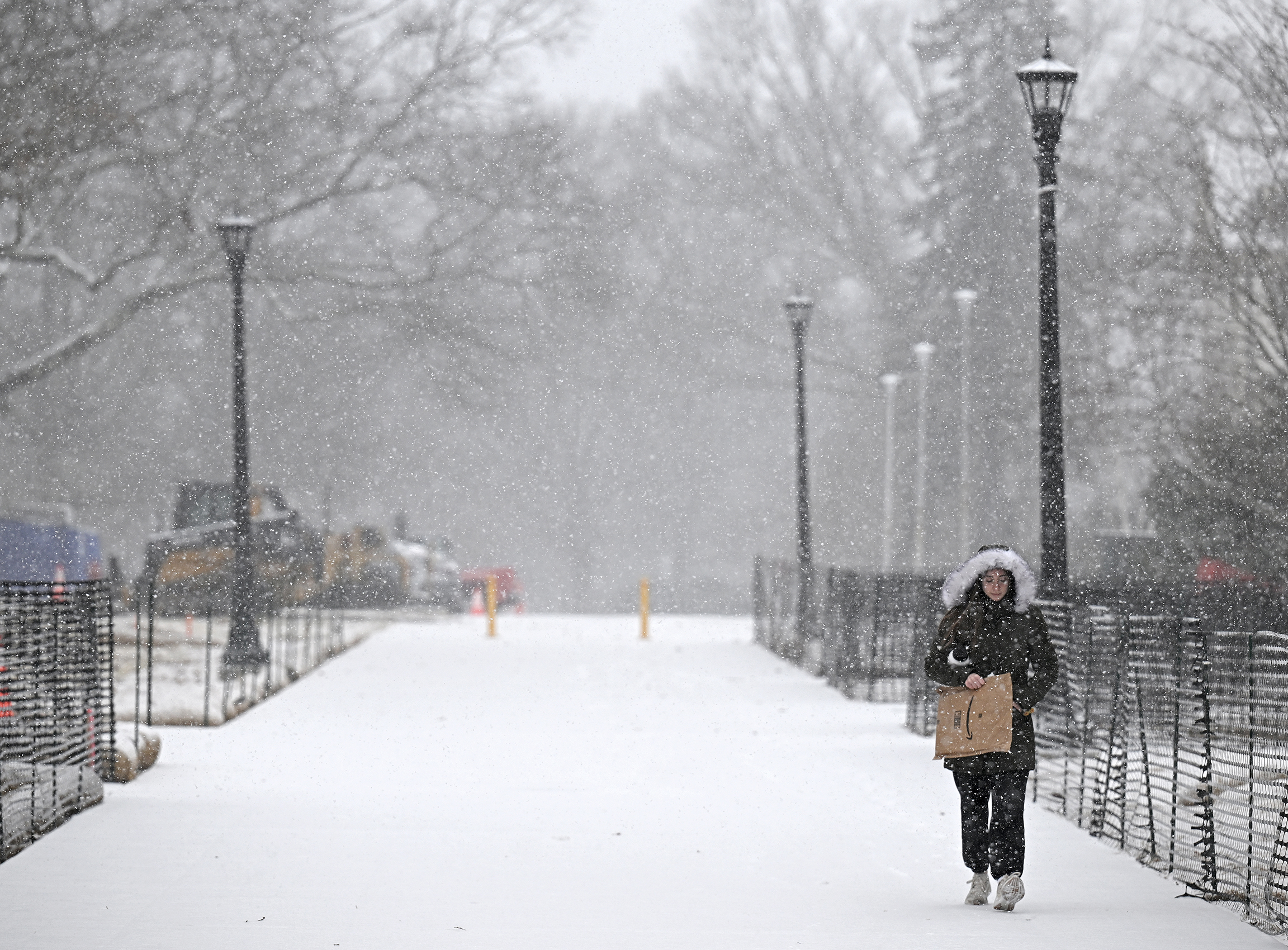 A student in a hooded coat walks along a pedestrian promenade in a snowstorm.