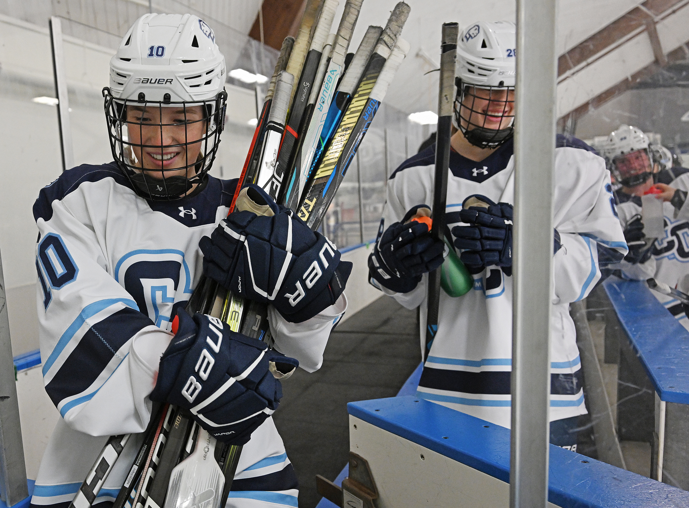 A female hockey player gathers hockey sticks to carry them out of the bench area following a hockey game.