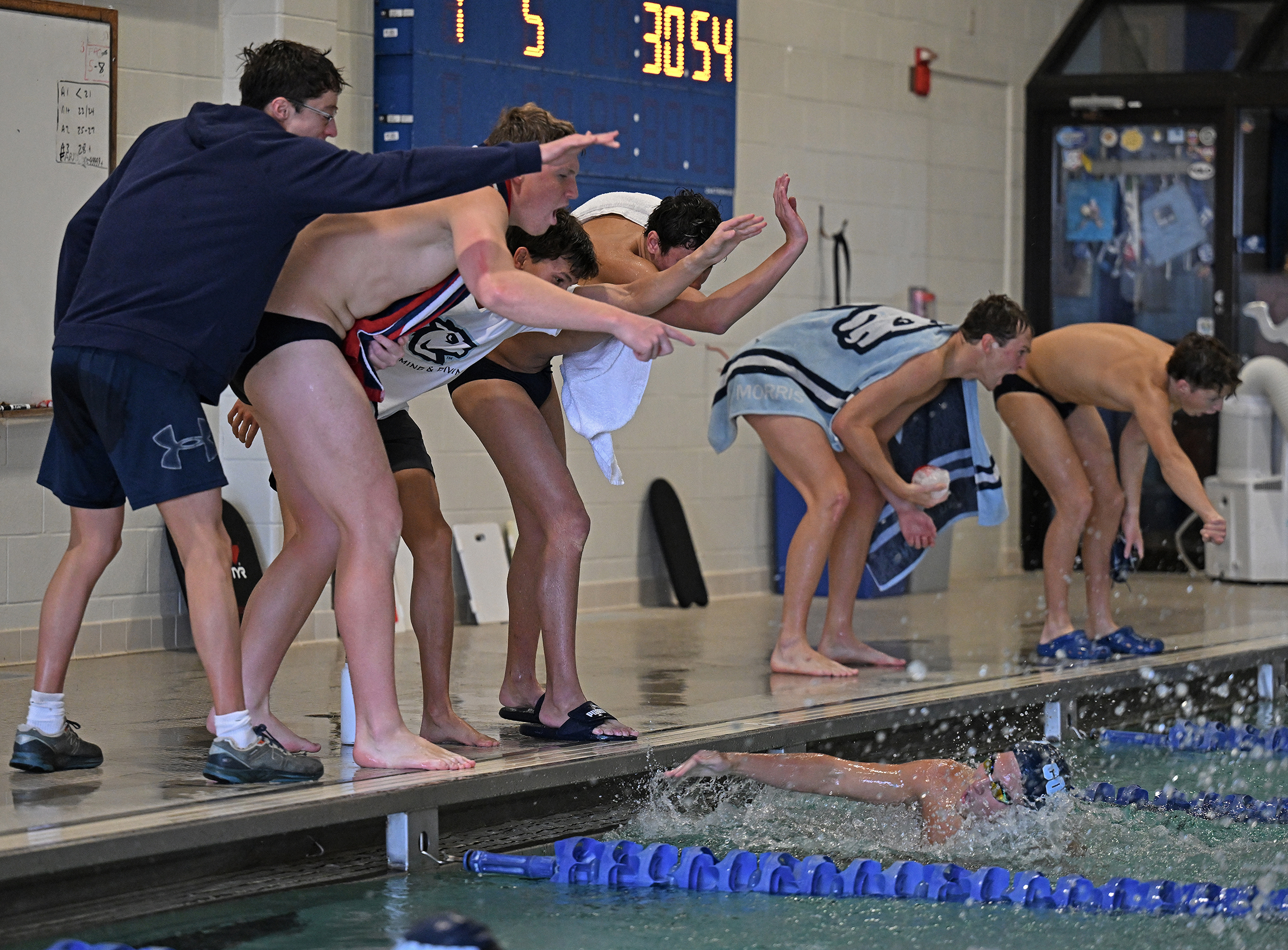 A group of swimmers cheer from poolside as a teammate competes in a butterfly stroke race.