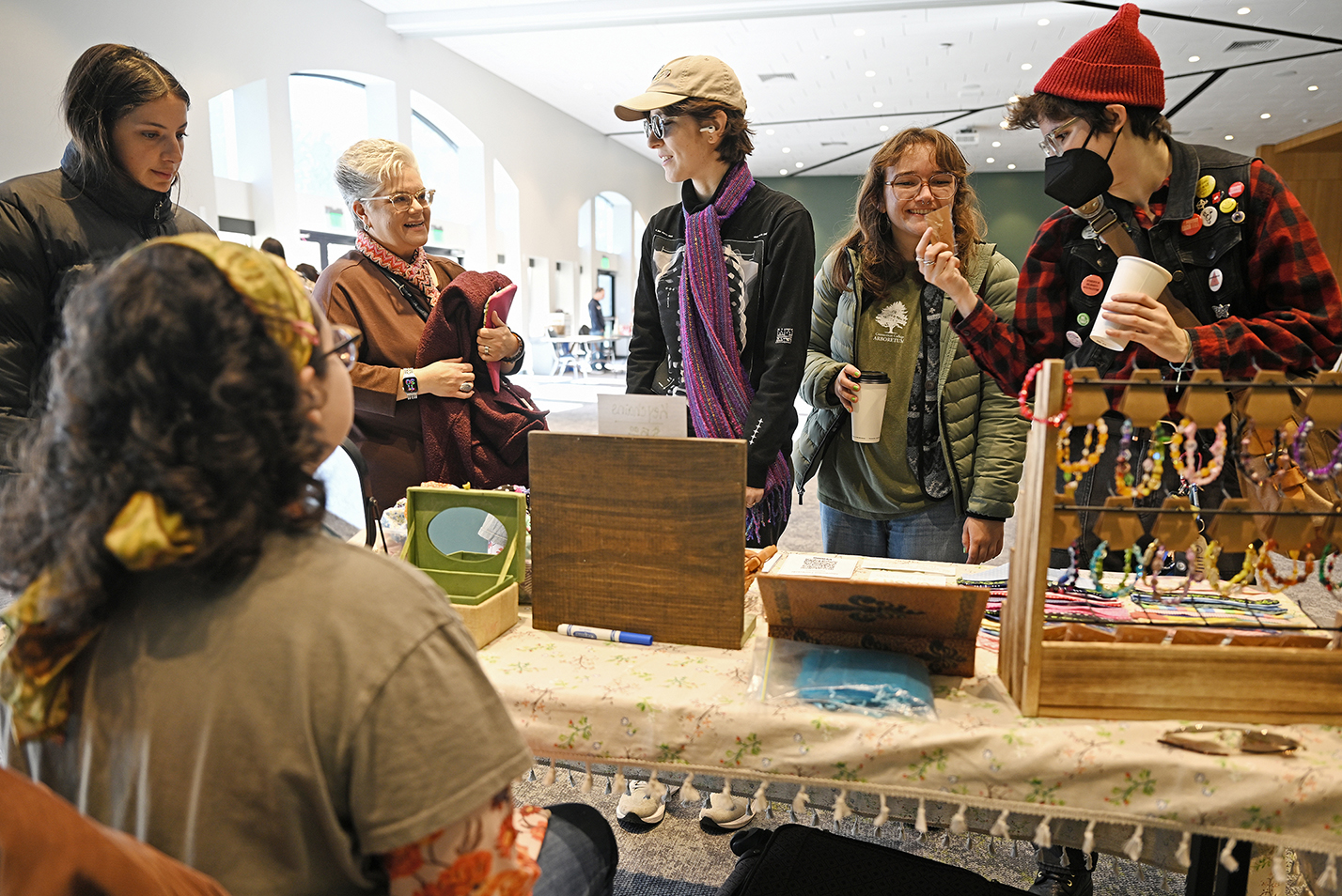 A group of customers look at the crafts on display at a vendor table during a craft fair.
