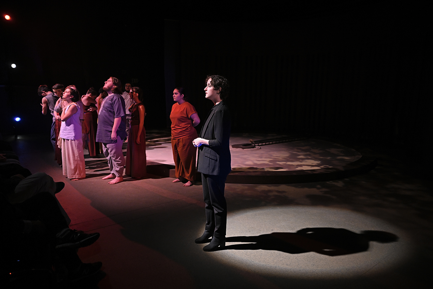 A student director stands in a spotlight and introduces the setting for a performance in a black box theater.