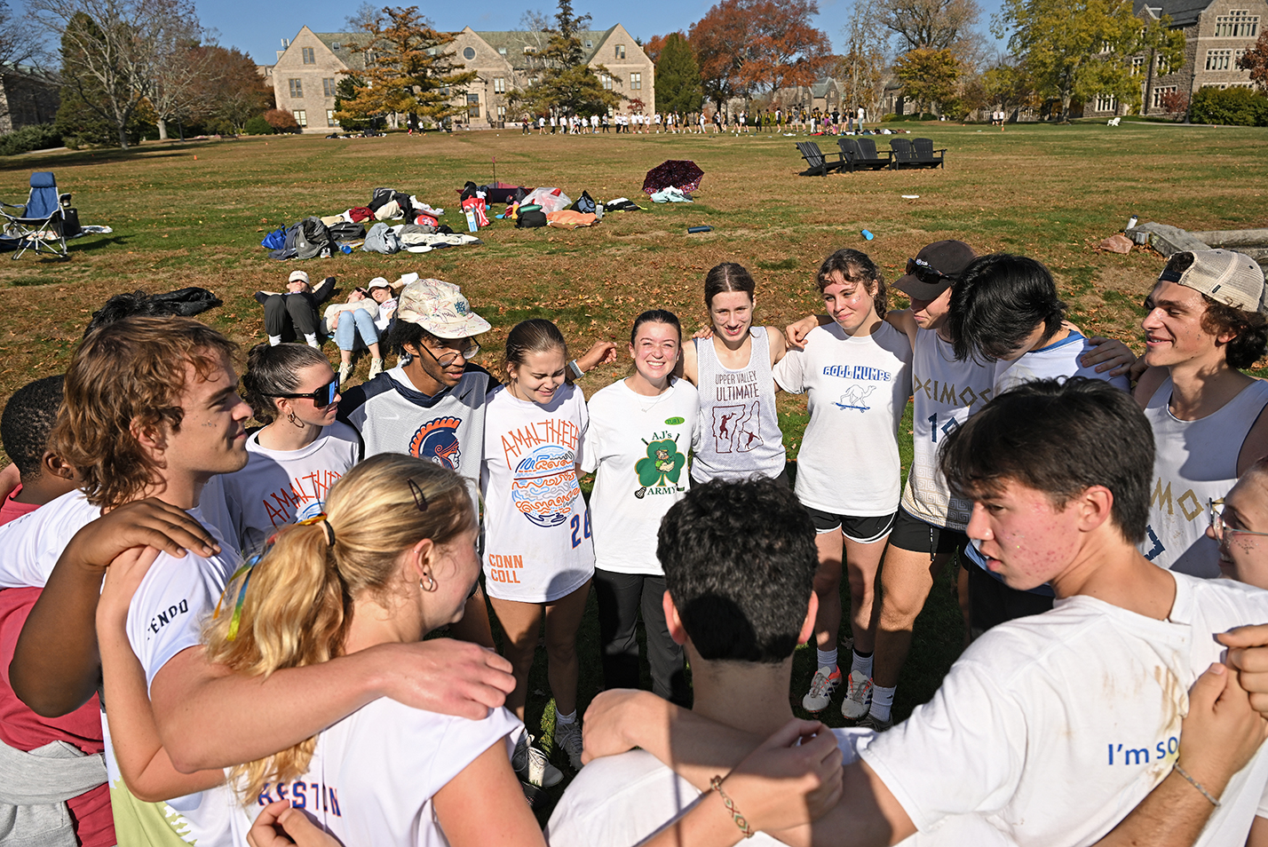 A college club sports team gathers in a circle to give a cheer on a college green on a sunny day.