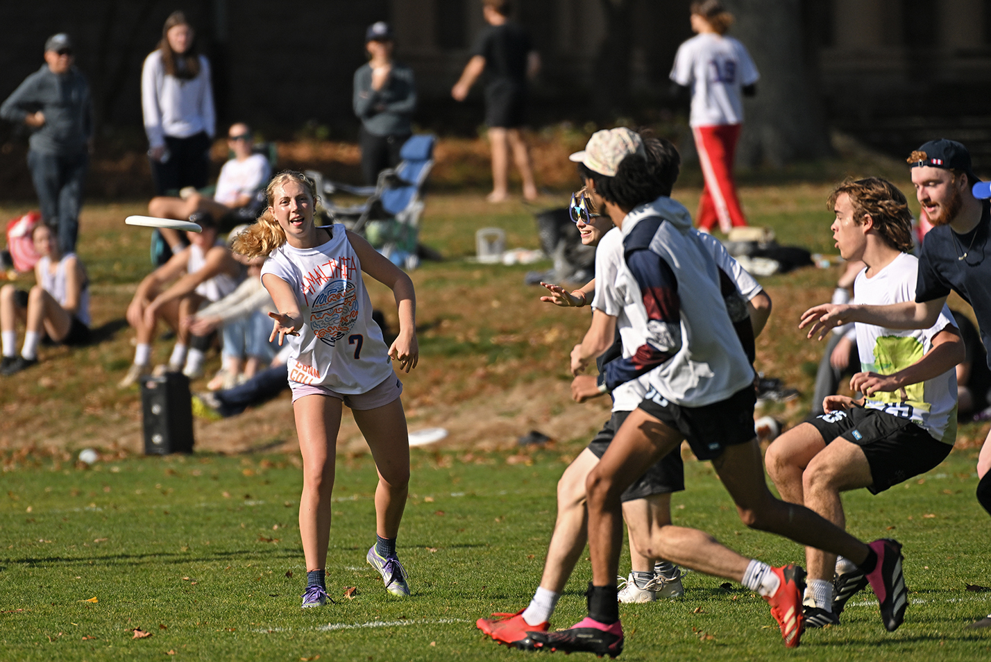 A college ultimate disc player throws the disc downfield into a crowd of players.