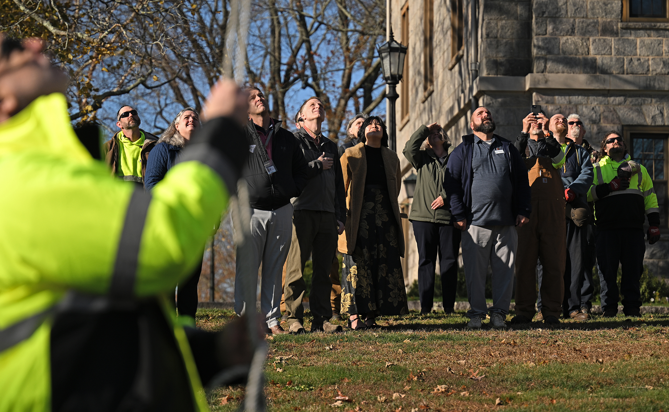 A group of people stand and look up as they watch the U.S. flag raised for Veterans Day.
