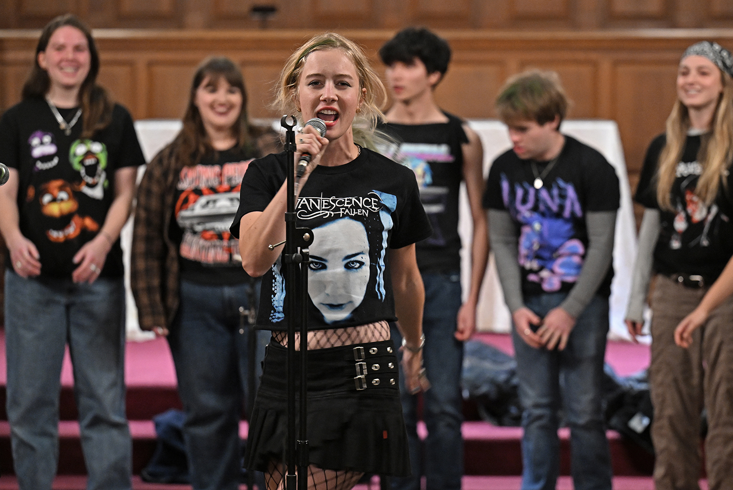 A soloist stands in front of a college a cappella group singing into a microphone.