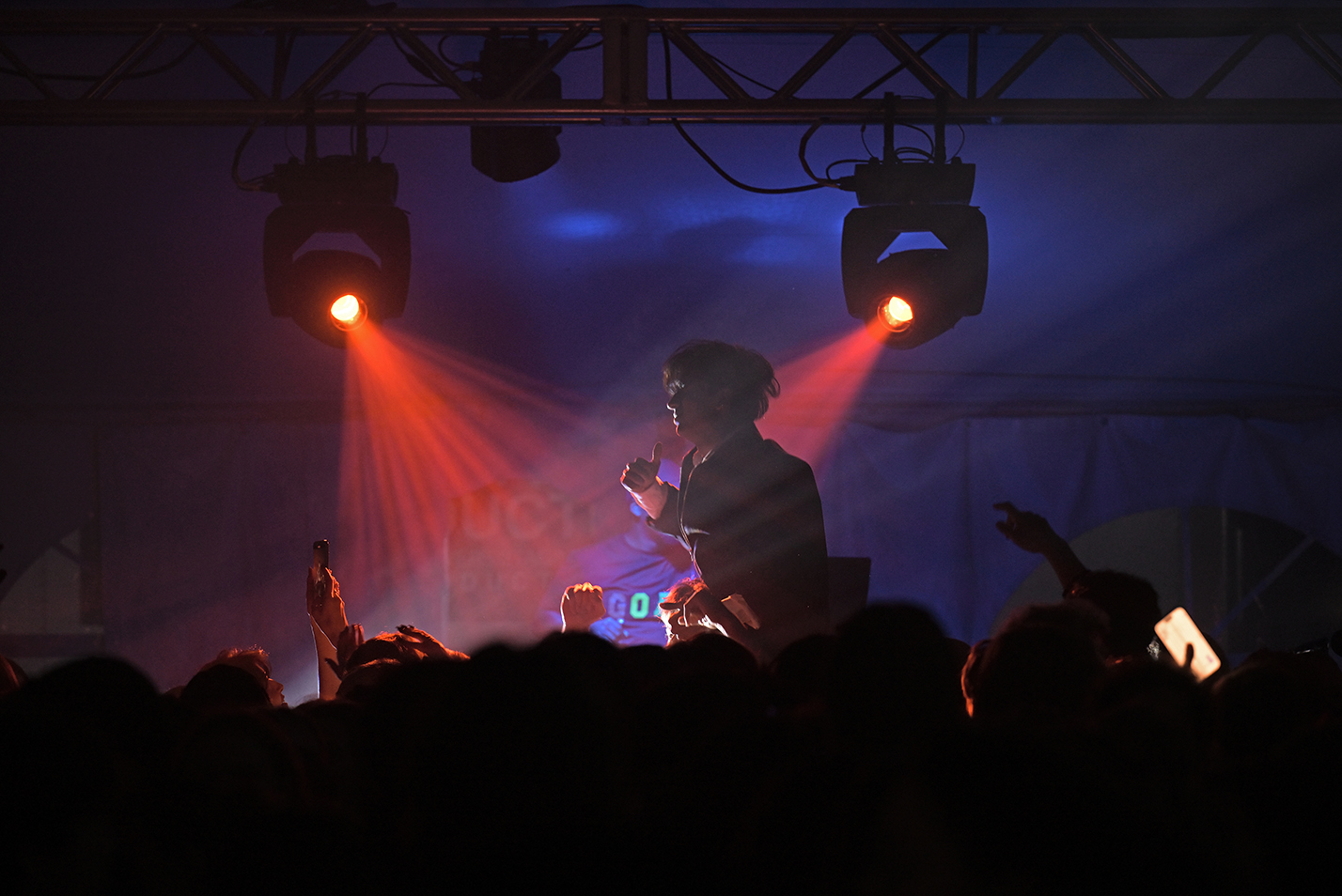 A student lit by spotlights dances while seated on a friend's shoulders over a crowd at a college dance party.