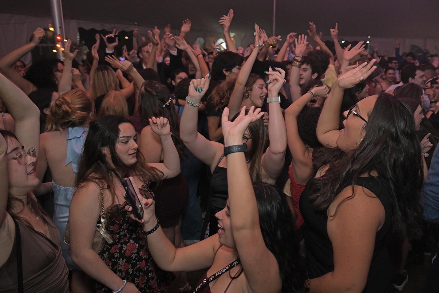 A large crowd of students with arms raised fill a dance floor.