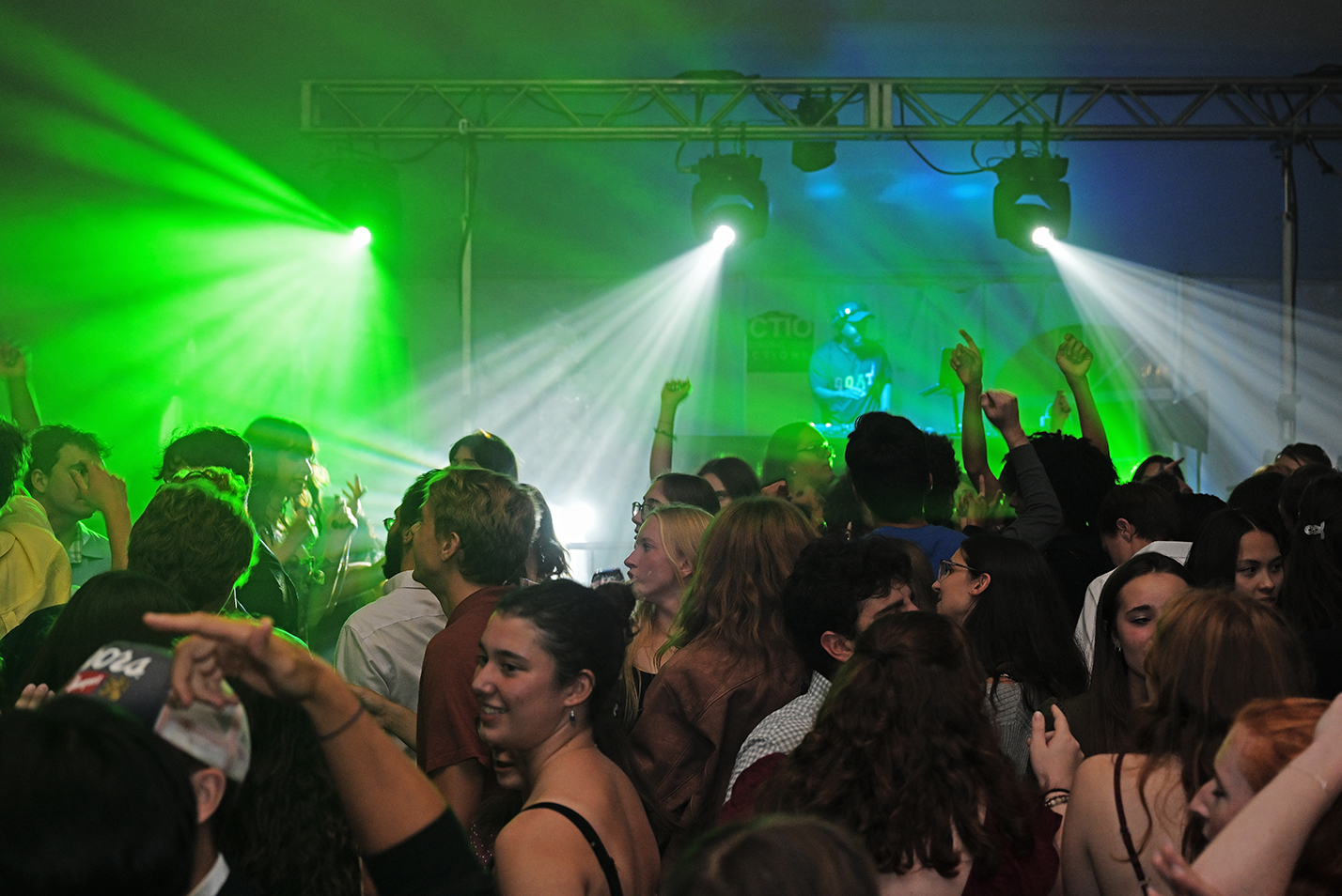 A large crowd of students fill a dance floor lit by green and blue spotlights.