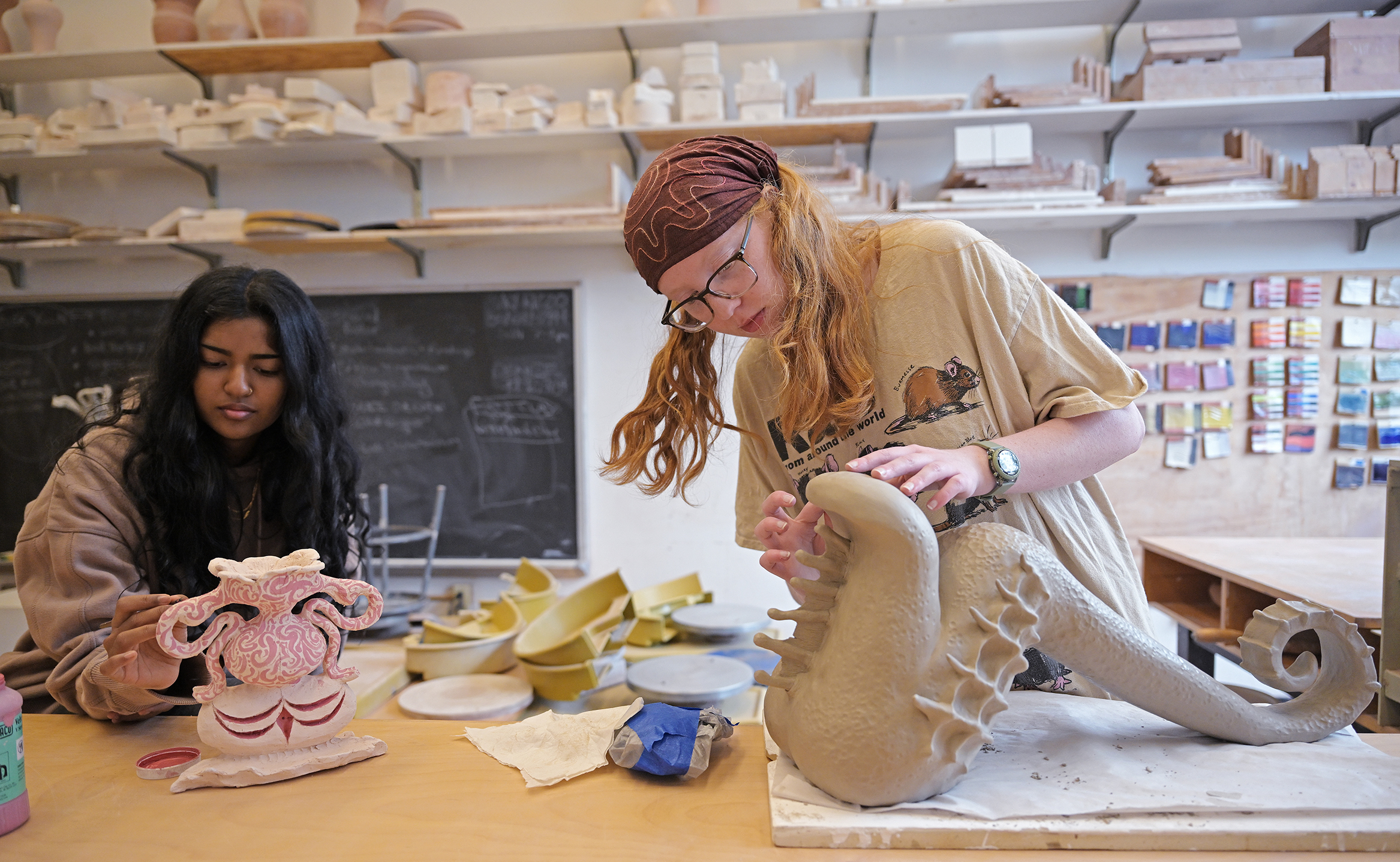 Two student artists work on elaborate ceramic vessels in a college art studio.
