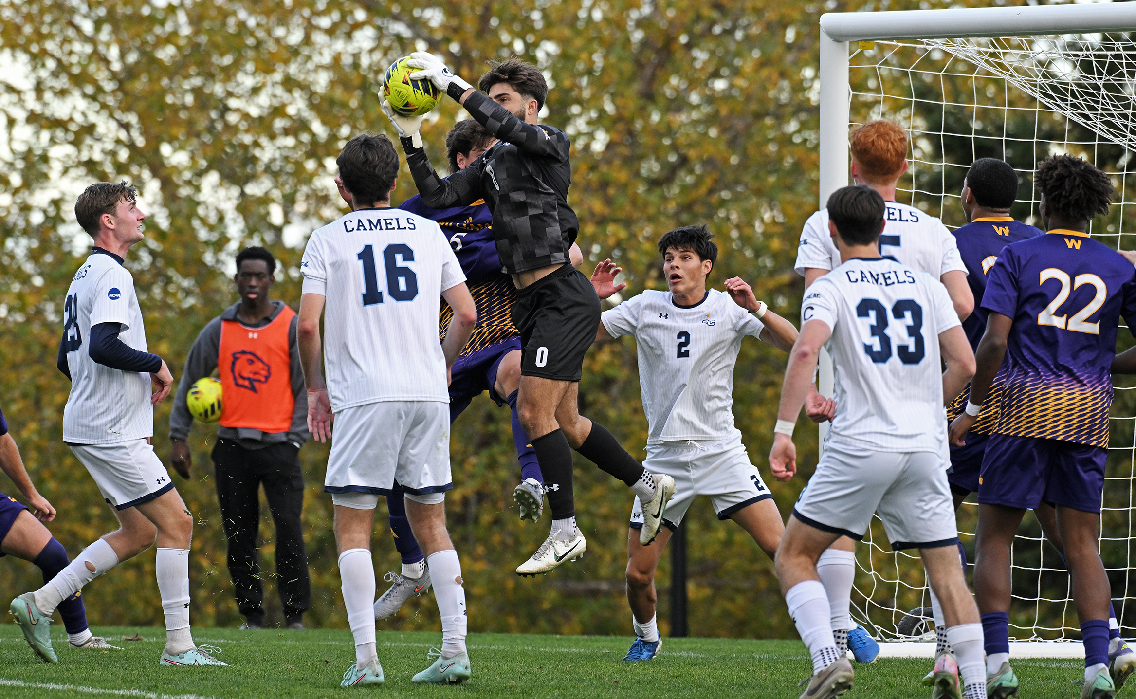 A college soccer goalie leaps into a crowd of players to grab the ball. out of the air.