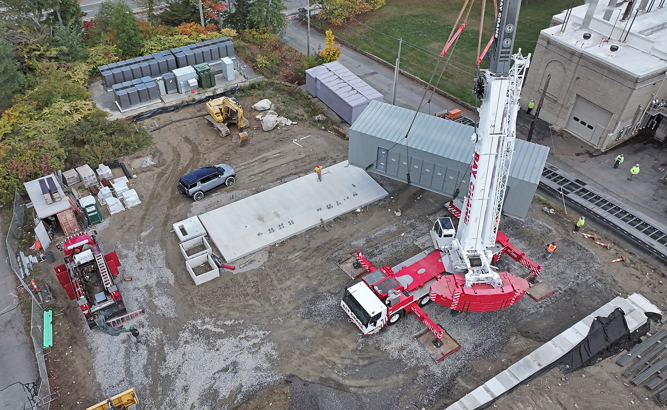 An aerial view of a heavy-lift crane moving a modular building off a trailer and onto a concrete foundation.