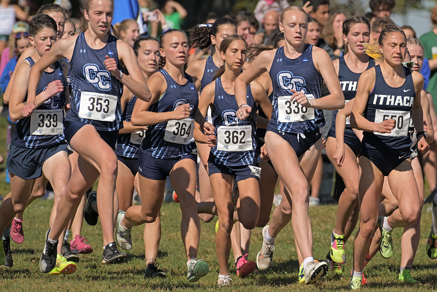 Female collegiate cross country runners take off in a mass start on a sunny fall day.