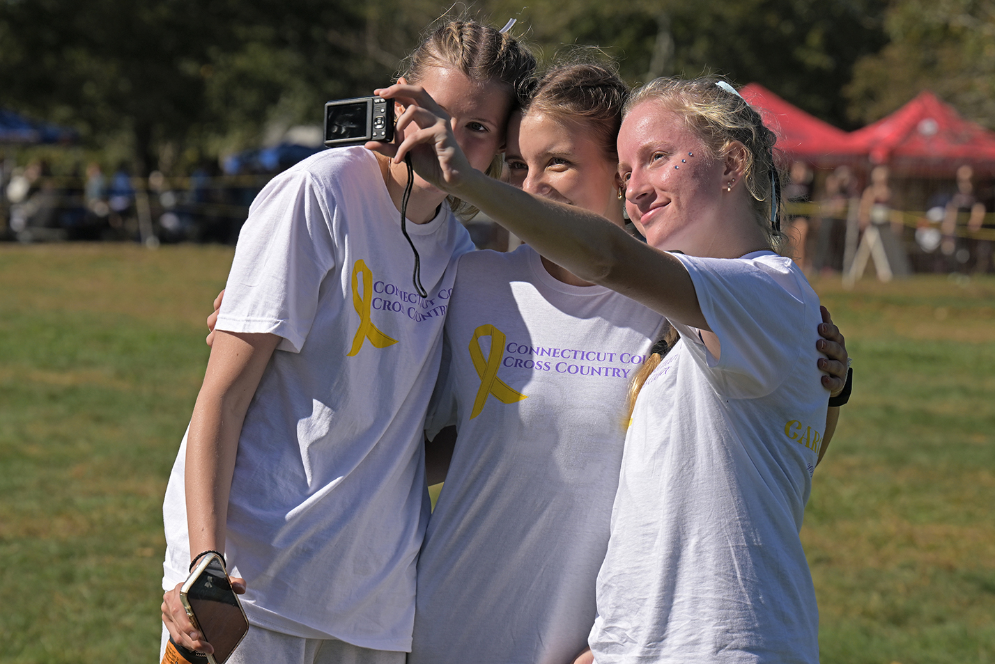 Three female college cross country runners take a photo together after competing in a race.