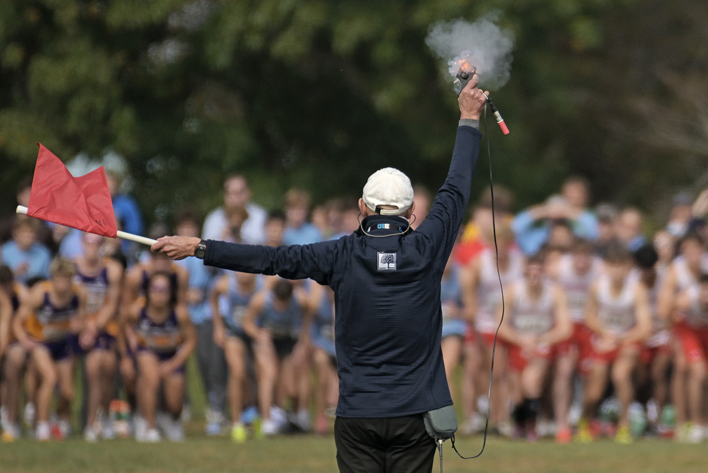 Orange flame bursts from the starter's pistol as a collegiate cross country running race mass start gets under way.