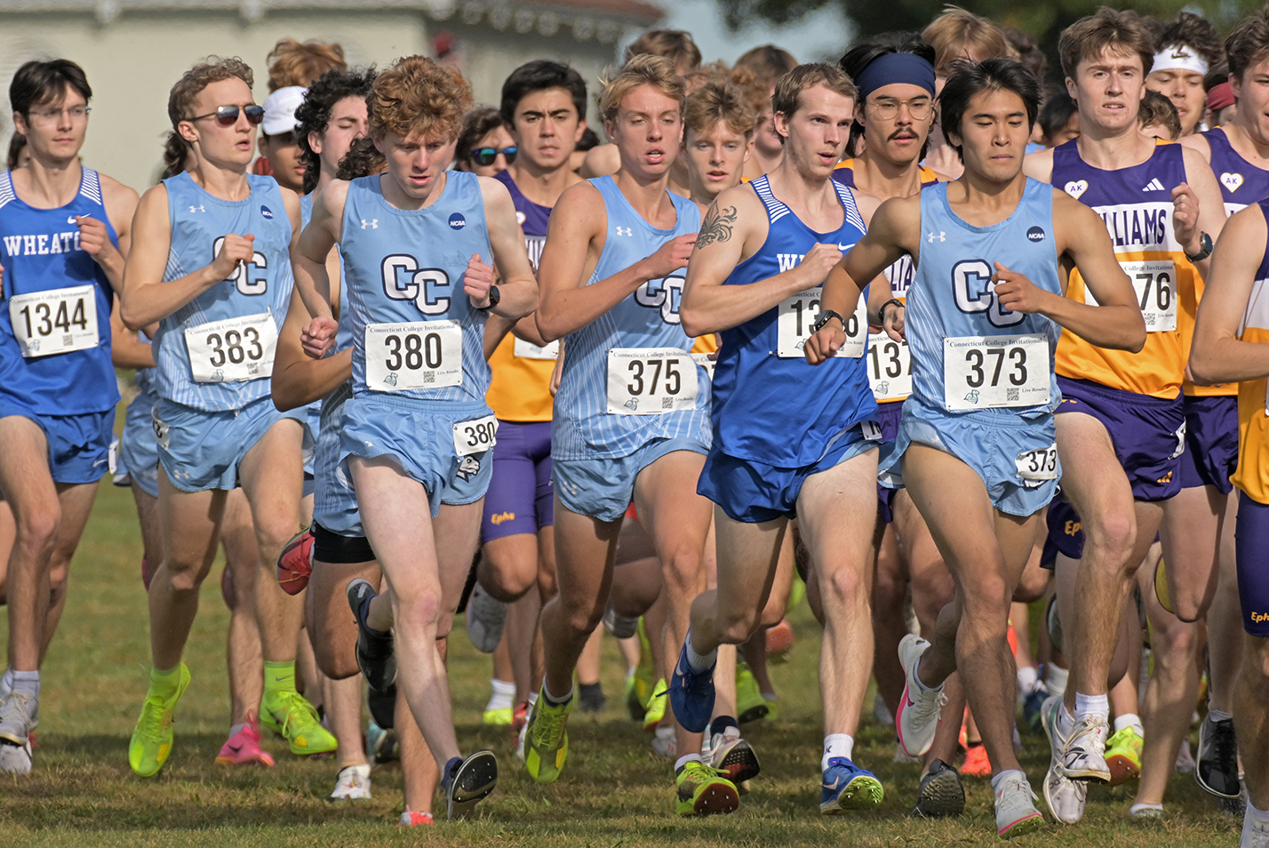 Male collegiate cross country runners take off in a mass start on a sunny fall day.
