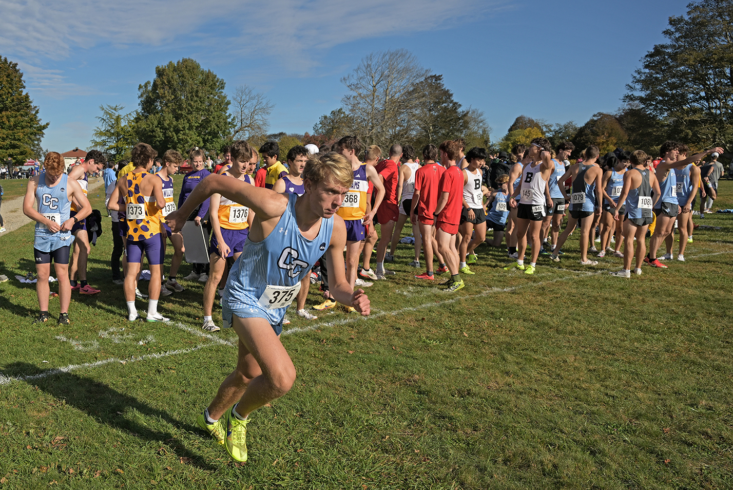 A male cross country runner in light blue uniform takes a practice start before a race.