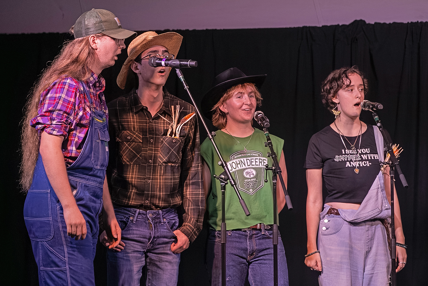 a college a cappella group dressed in farm costumes performs on stage.