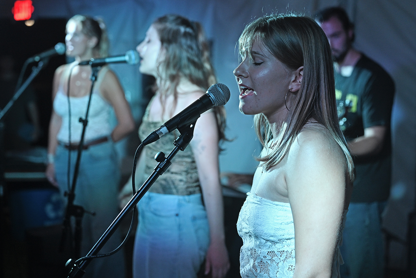 Three female student singers perform with a band on a stage.