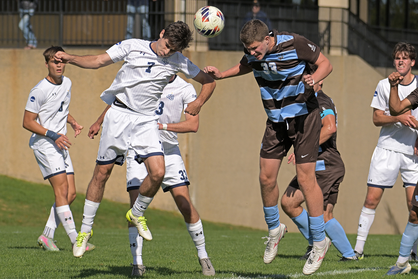Two soccer players leap into the air in an attempt to head the ball during a college soccer match.