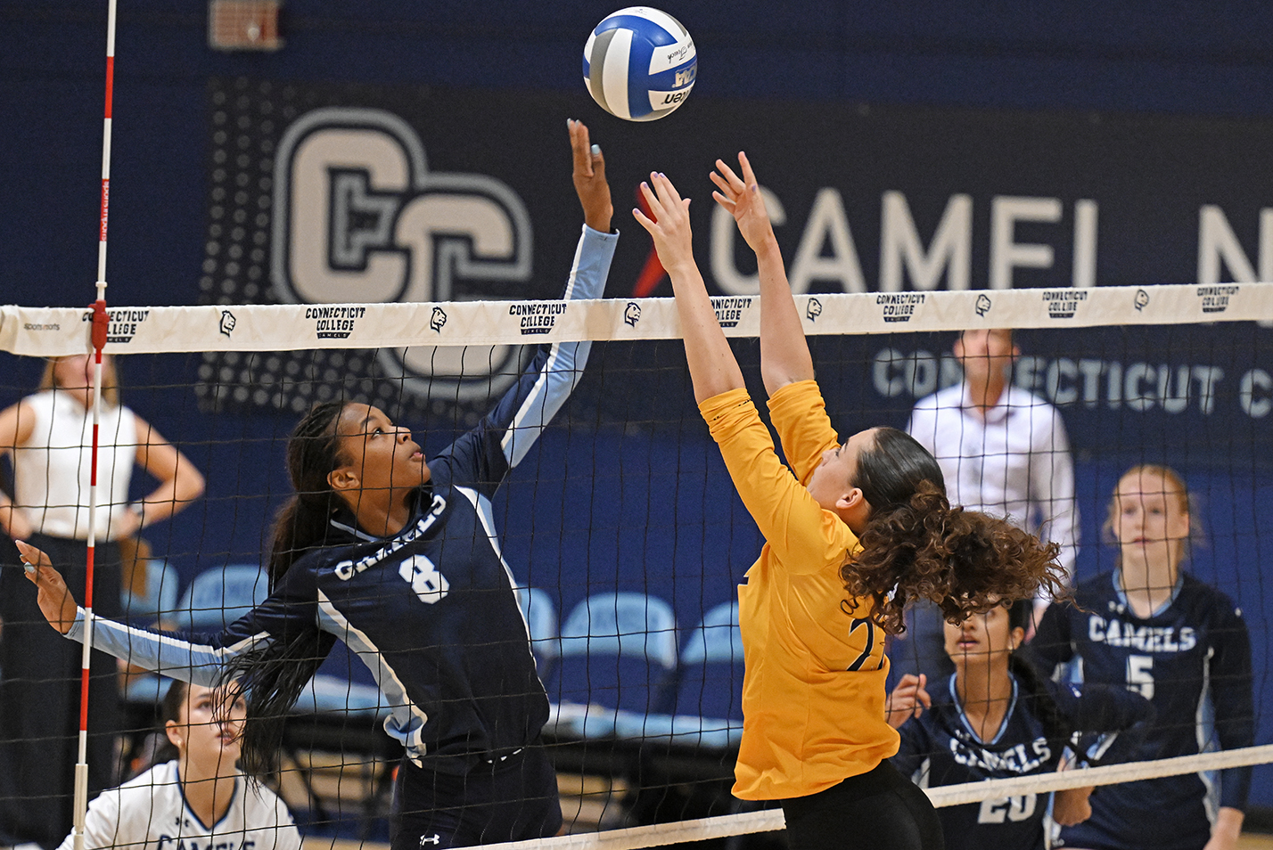 Two female college volleyball players vie for control of the ball at the net.