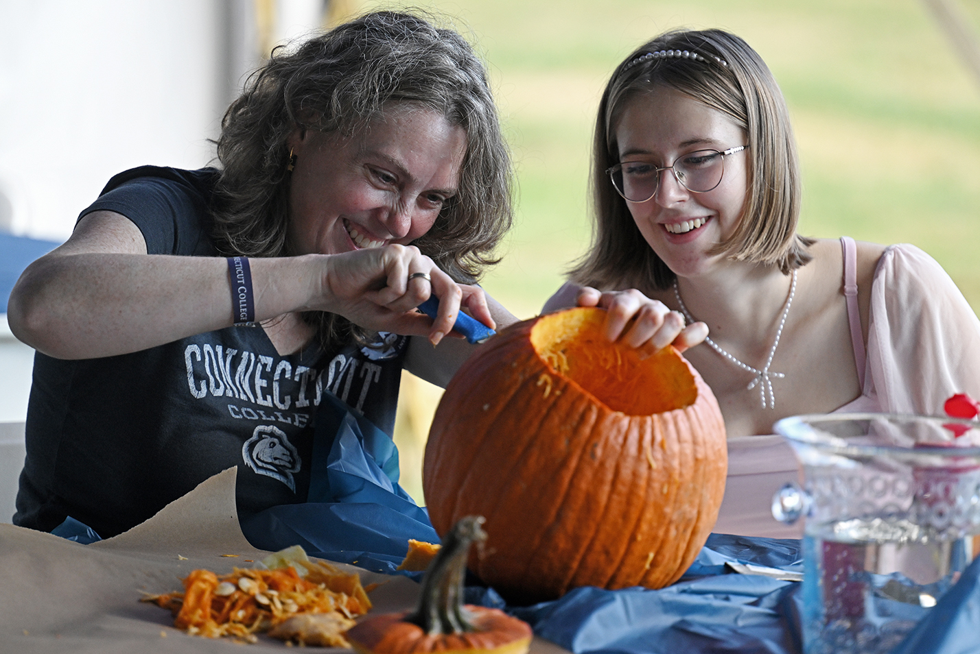 A woman and her college-age daughter smile as they carve a pumpkin into a jack-o-lantern.