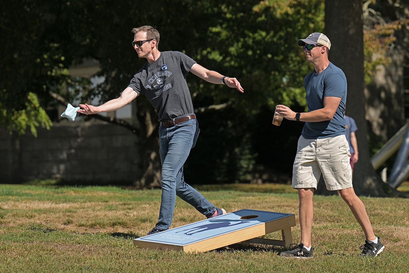 Two men play cornhole on a college green.