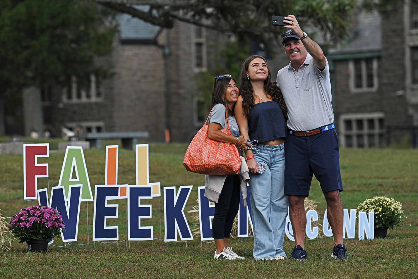 A couple and their college-age daughter take a selfie-photo in front of the words 