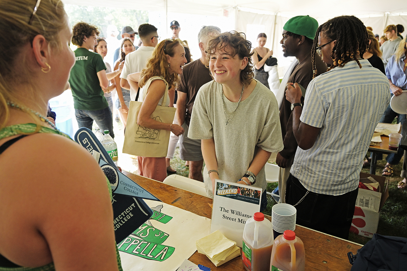 A college student give a big smile to a friend visiting them during an open house style event under a big top tent.