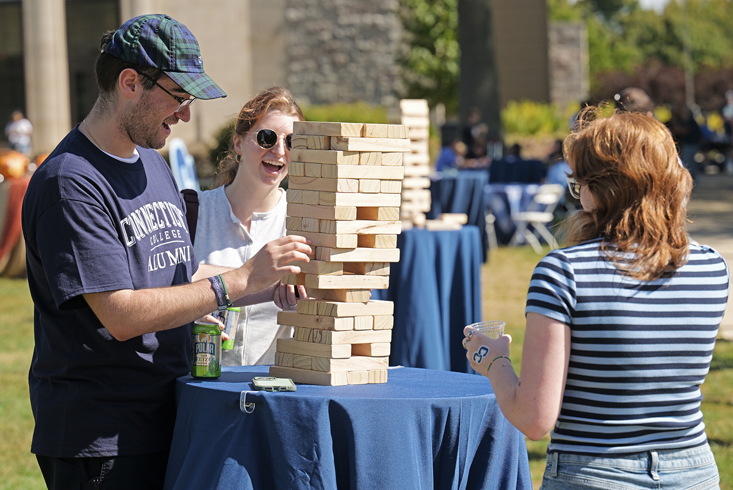 A trio of college alumni play a wood block stacking game outdoors.