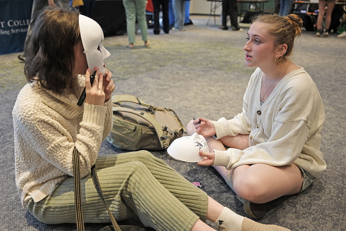 Two female college students sit on the floor and decorate theatrical masks.