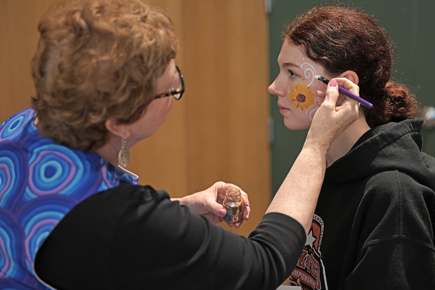 A student has her face painted with a swirling floral design.