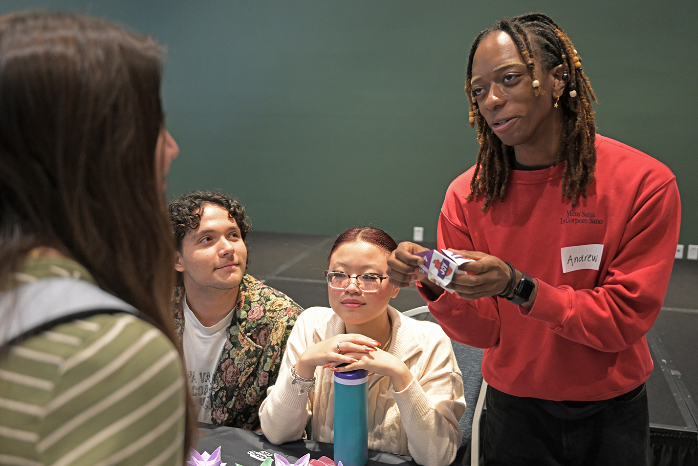 A college student with braided hair speaks to a student visiting their information table during a wellness fair.