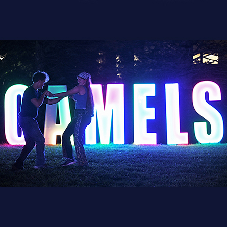 Students dance in front of a glowing Camels sign during Welcome Weekend.