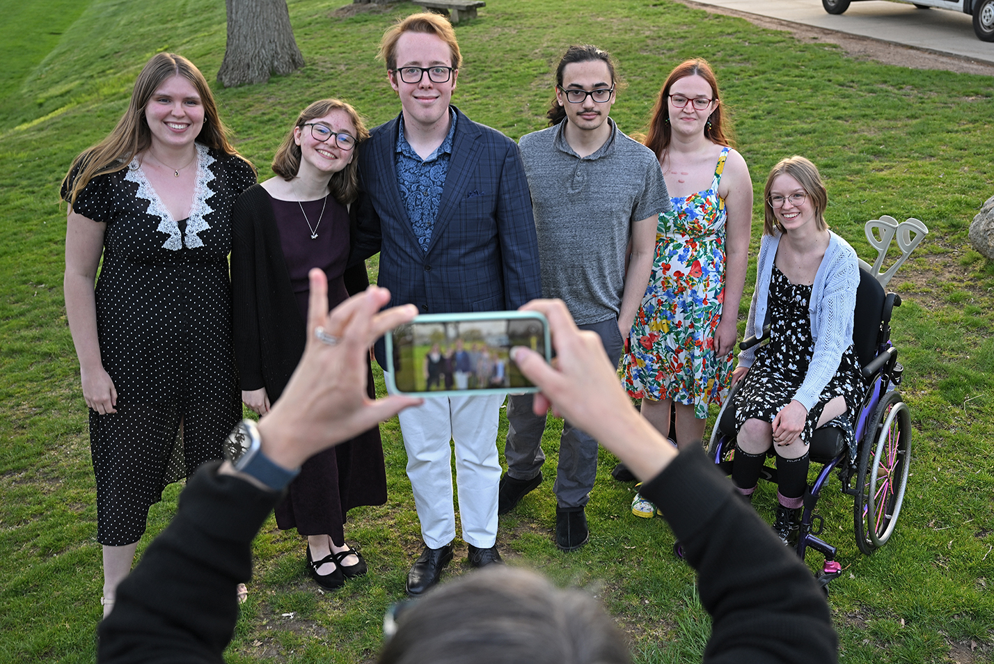 A group of college students stand together as a person with a smart phone takes their photo.
