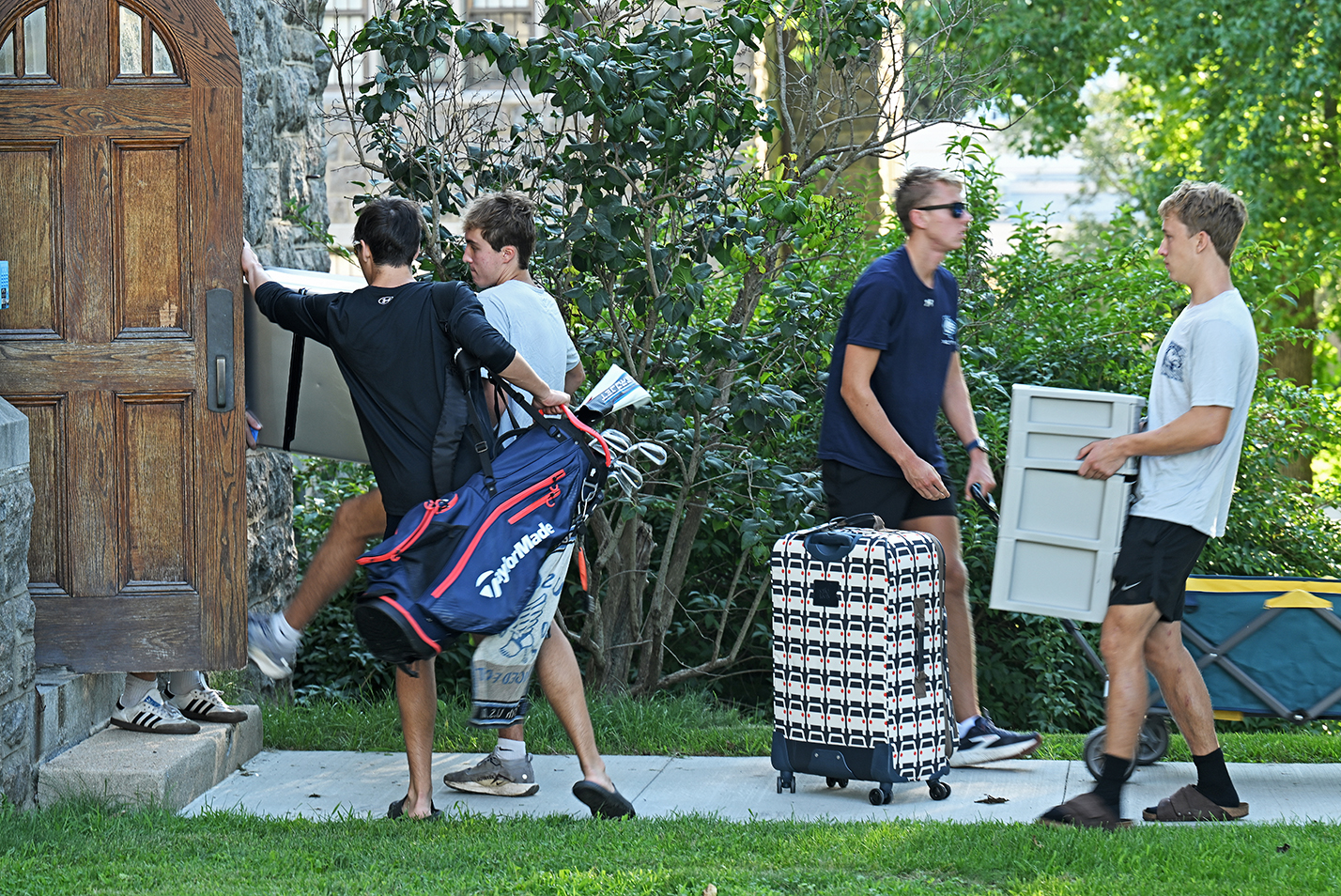 One student holds the door as a queue of students carrying items file into a college residence hall on move-in day.