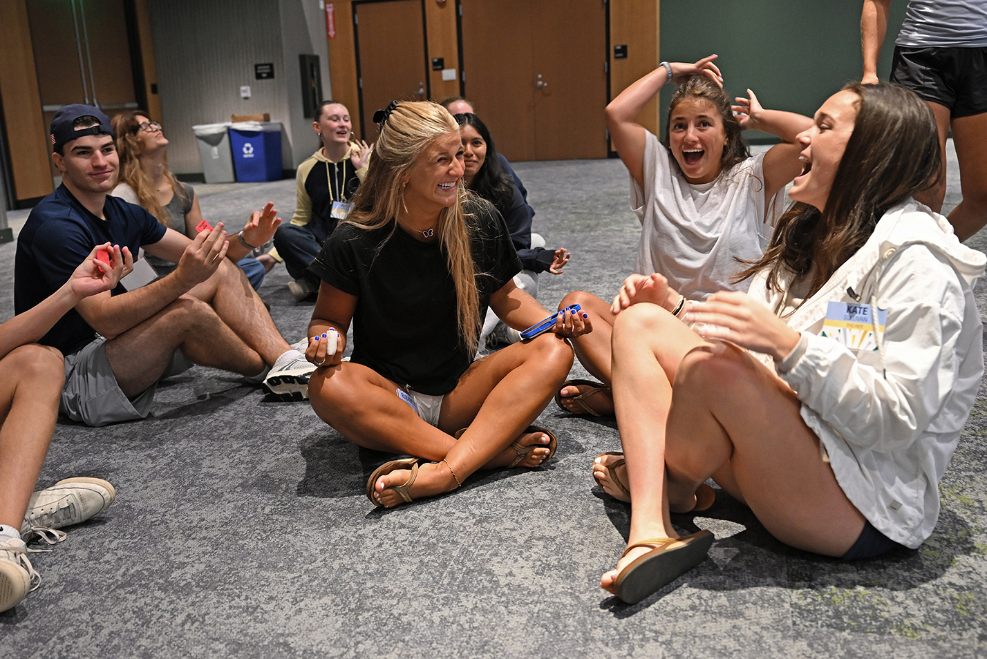 College students laugh as they sit on the floor in a large conference room during a team-building exercise.