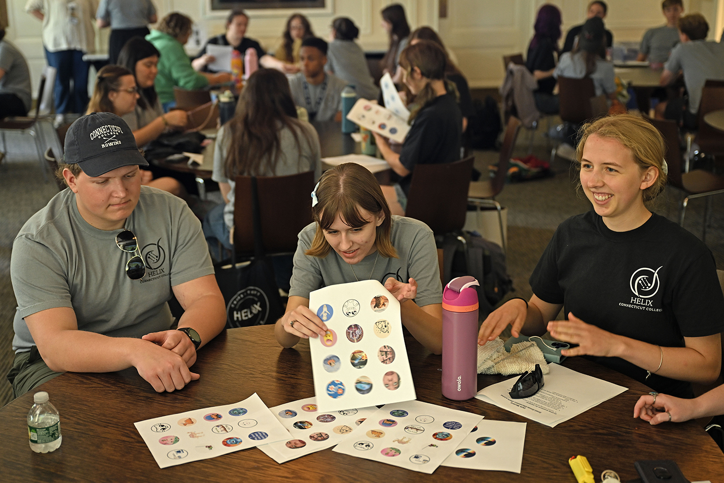 Students cut out small round graphics from sheets of paper during a button-making craft event.