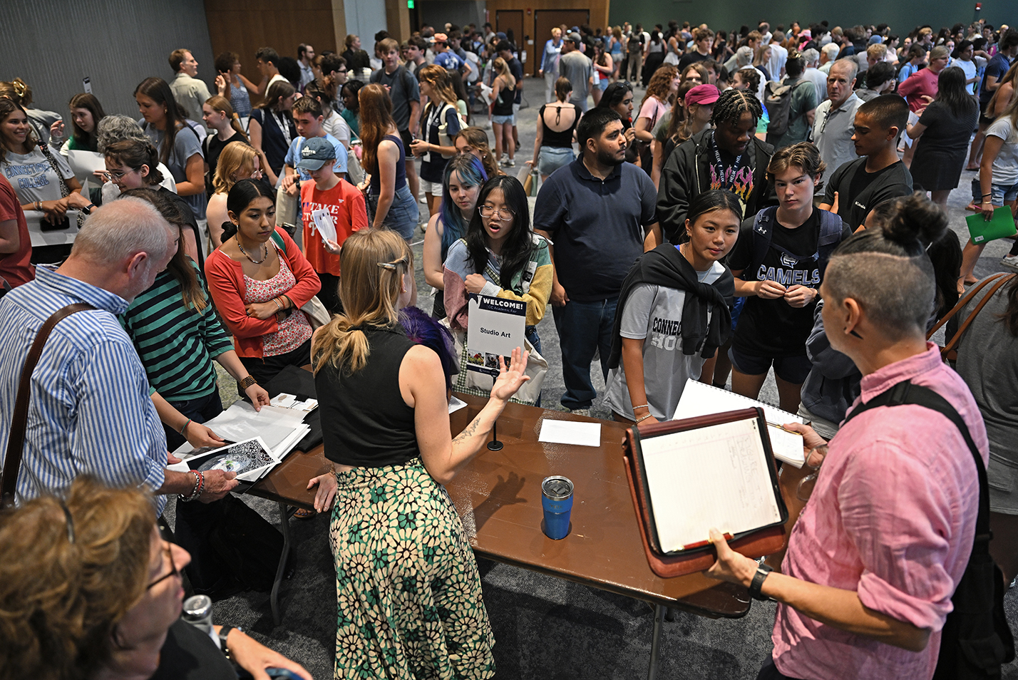 College students fill a conference room to meet professors at tables spread around the room.
