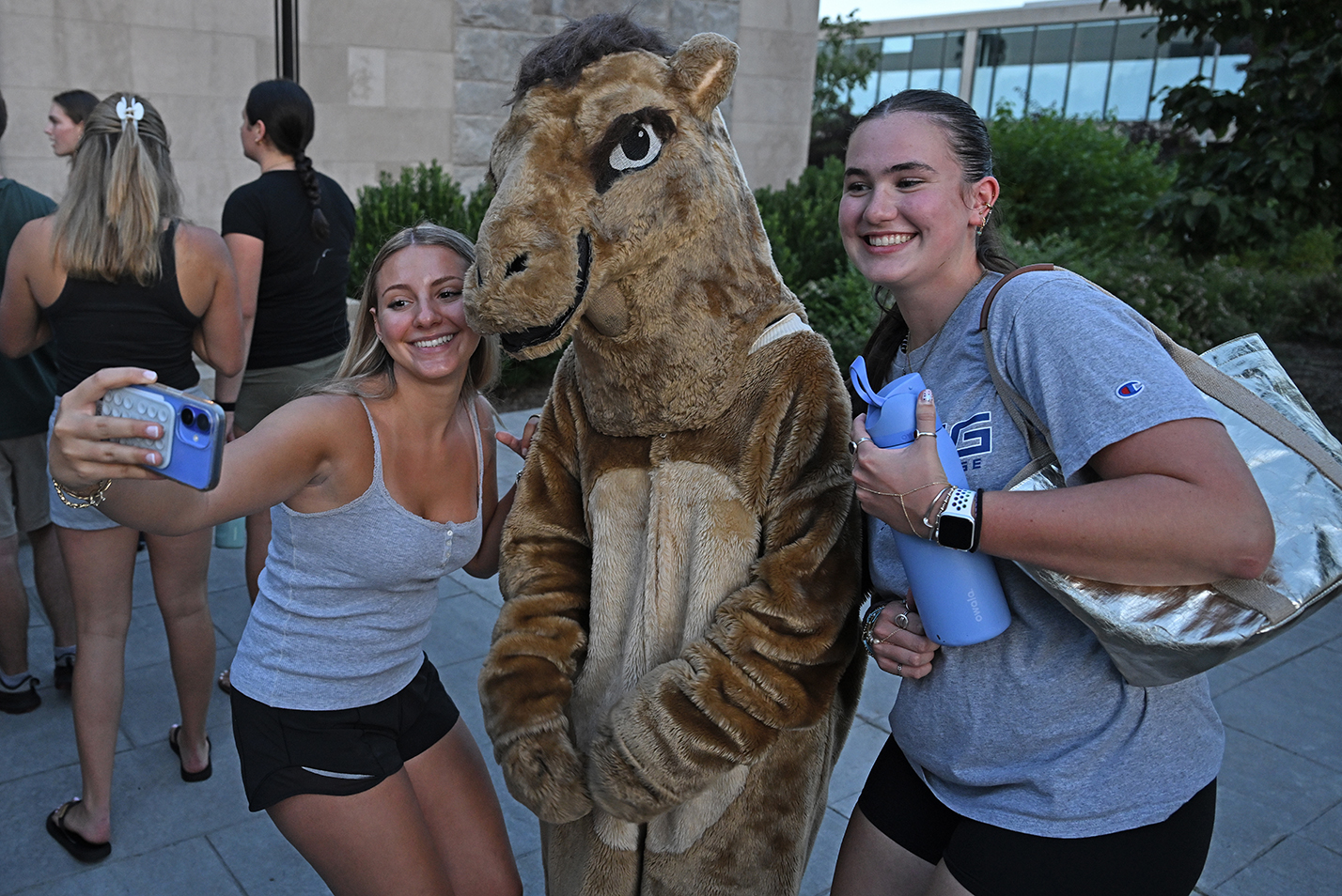 two female college students take a selfie photo with a student dressed in a camel mascot costume.