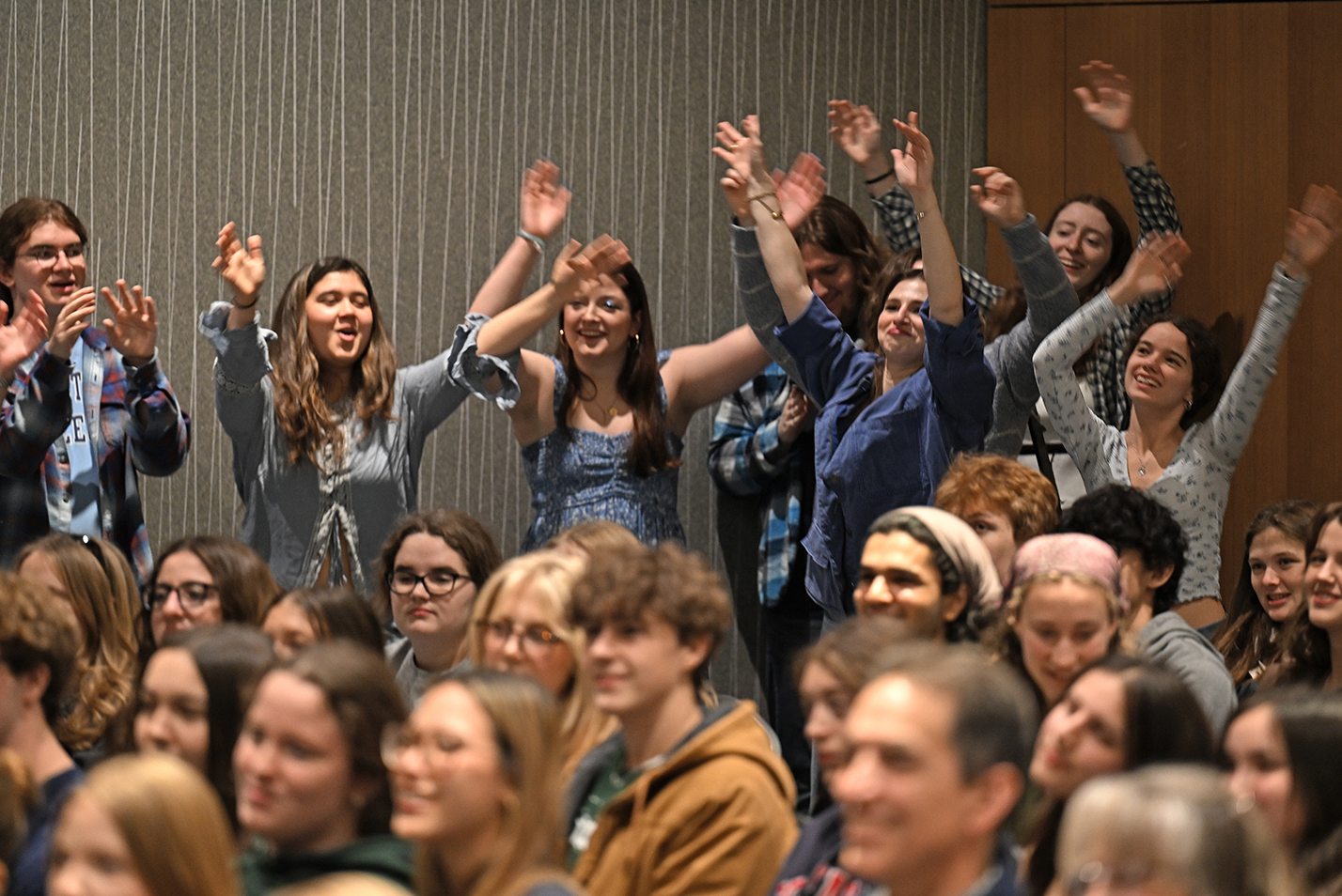 College students wave their hands in the air in the audience at an a cappella concert.