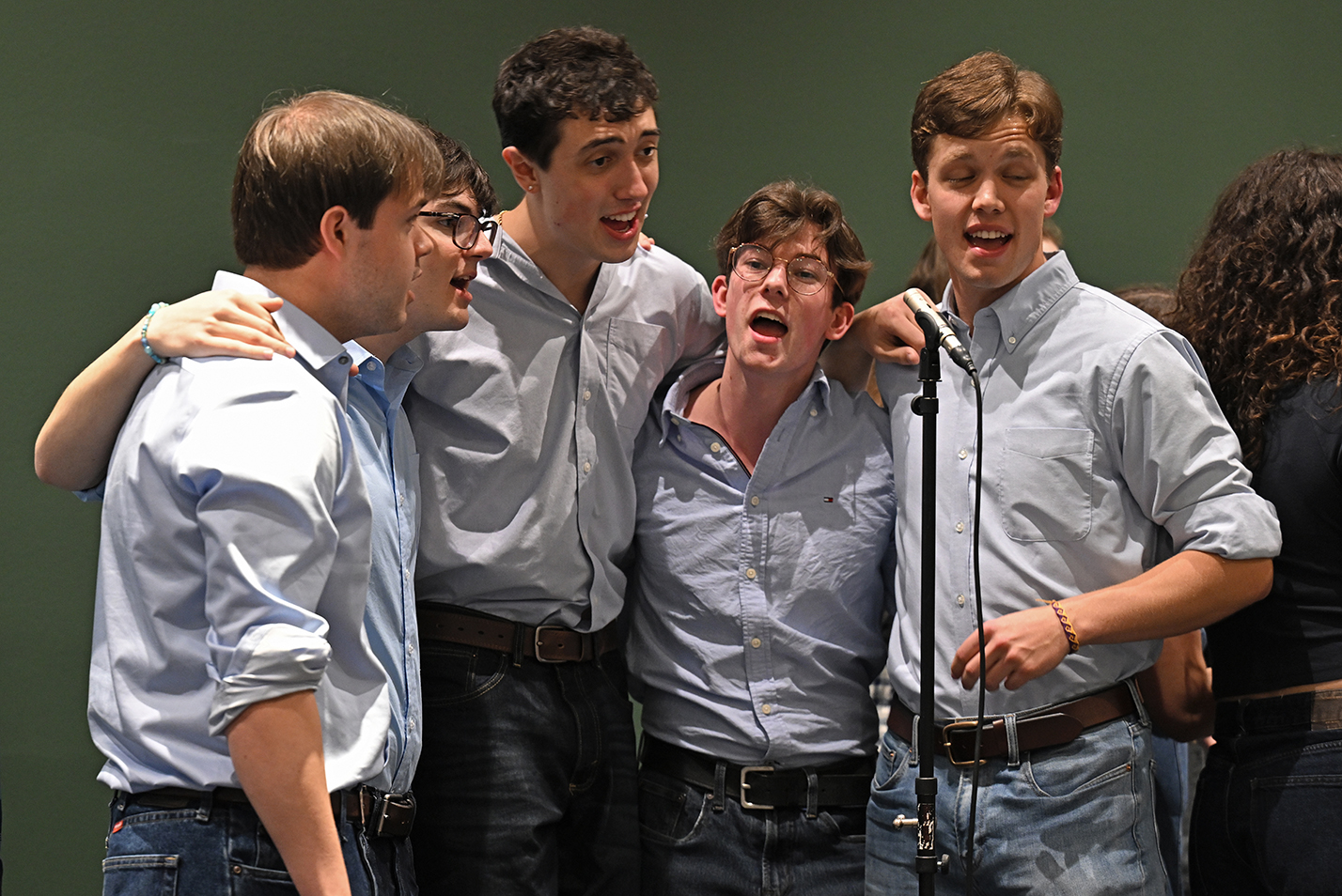 Four male a cappella singers in blue shirts and ties and arms around each other perform on stage.