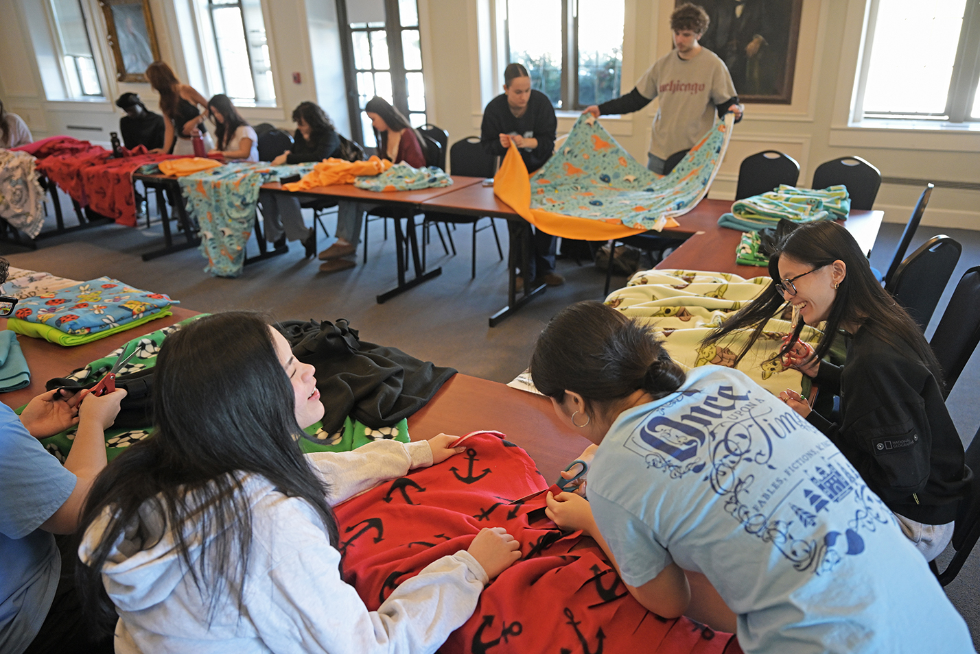 Students gathered around rows of tables handle fleece blankets.