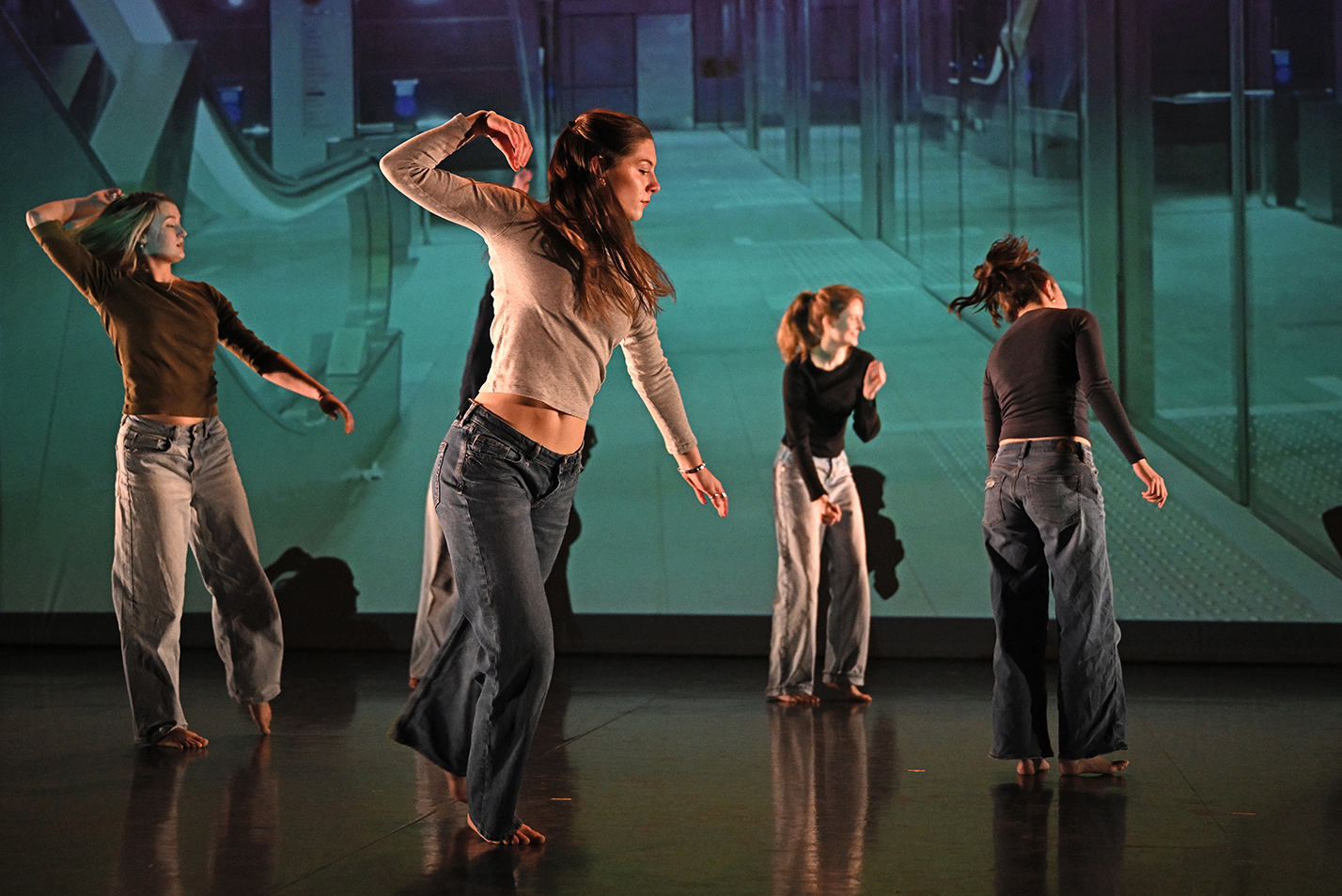 Student dancers perform in front of a projected scene in a college dance studio.