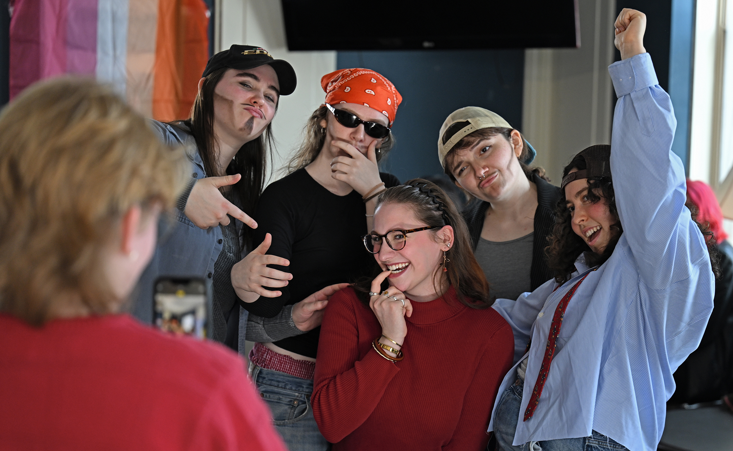 A student in a red shirt poses for a photo with a group of female students in male drag.
